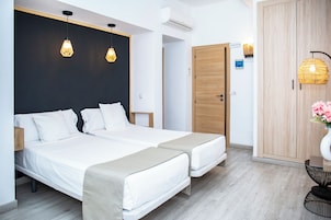 Moderni hotellihuone, jossa on kaksi sänkyä, puinen vaatekaappi ja pieni pöytä, jonka päällä on maljakko.