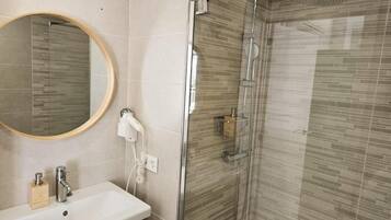 Un baño con ducha de vidrio, lavamanos con espejo y un armario de madera.