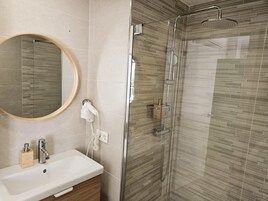 Un baño con ducha de vidrio, lavamanos con espejo y un armario de madera.