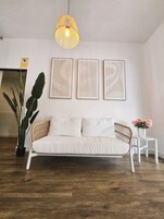 Een moderne woonkamer met een witte bank, een hanglamp en drie ingelijste kunstwerken aan de muur.