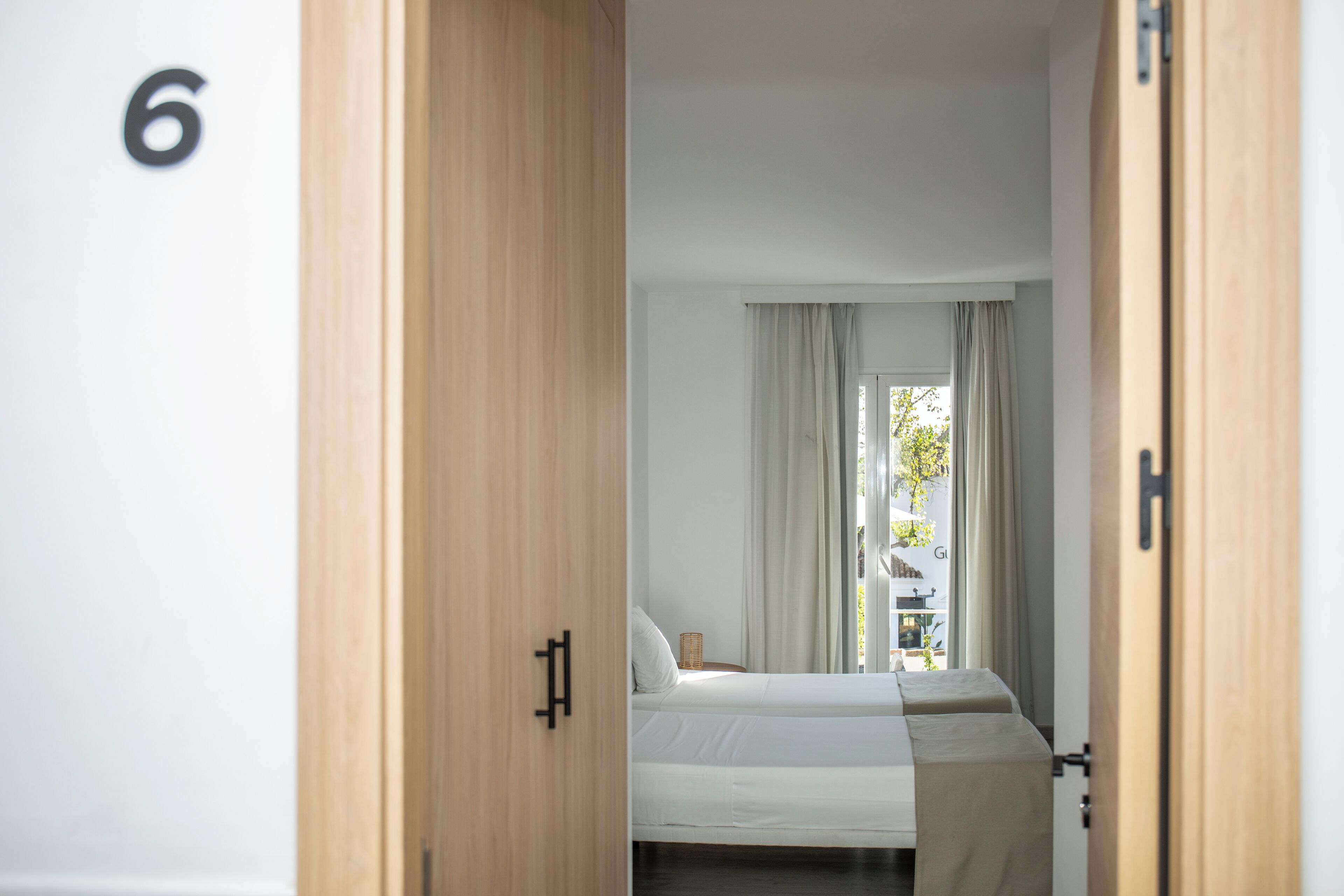 A bedroom with a bed, a wooden door, and a window with curtains.
