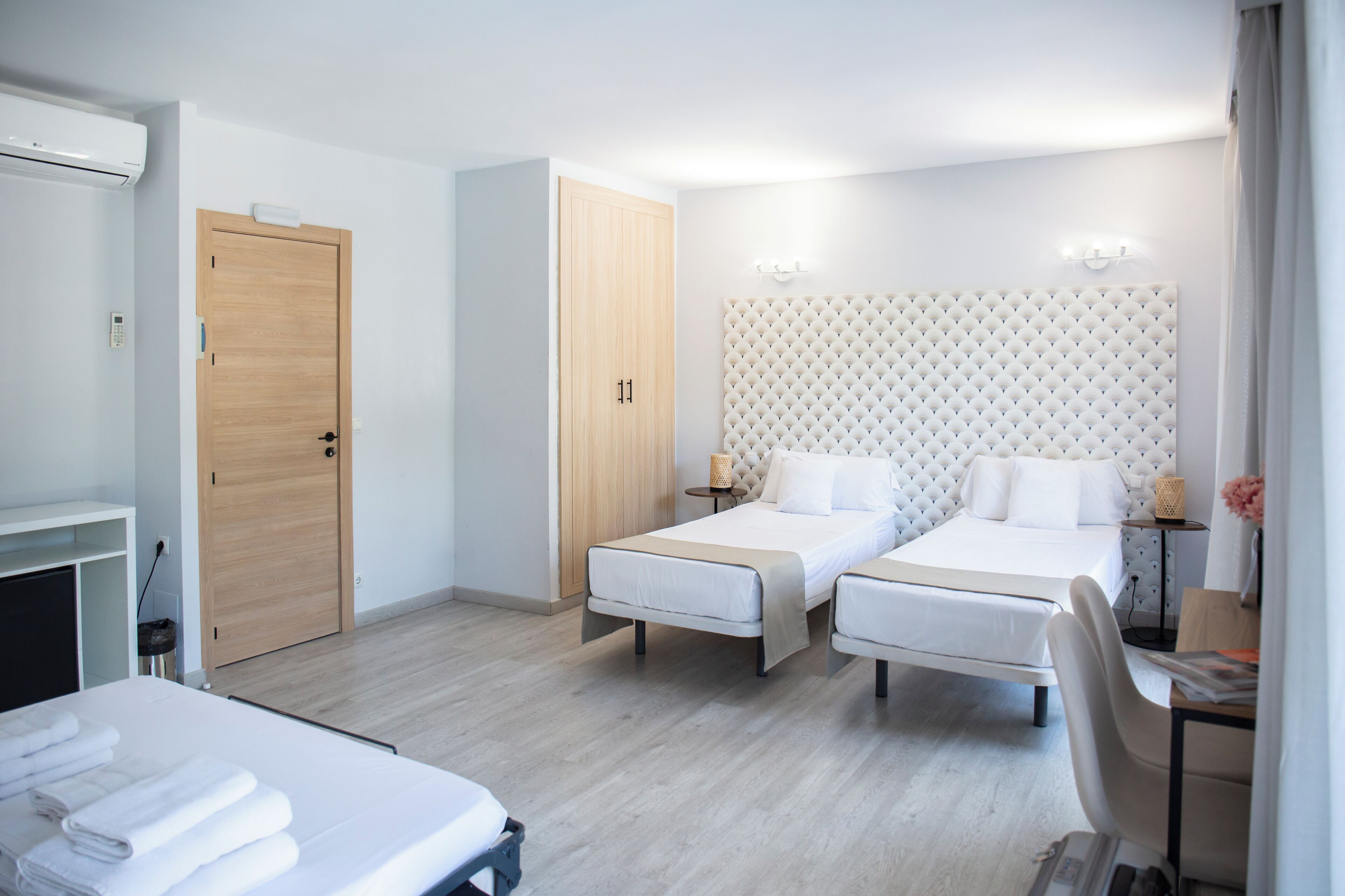 A hotel room with two beds, a desk, a chair, a wardrobe, and a bathroom.