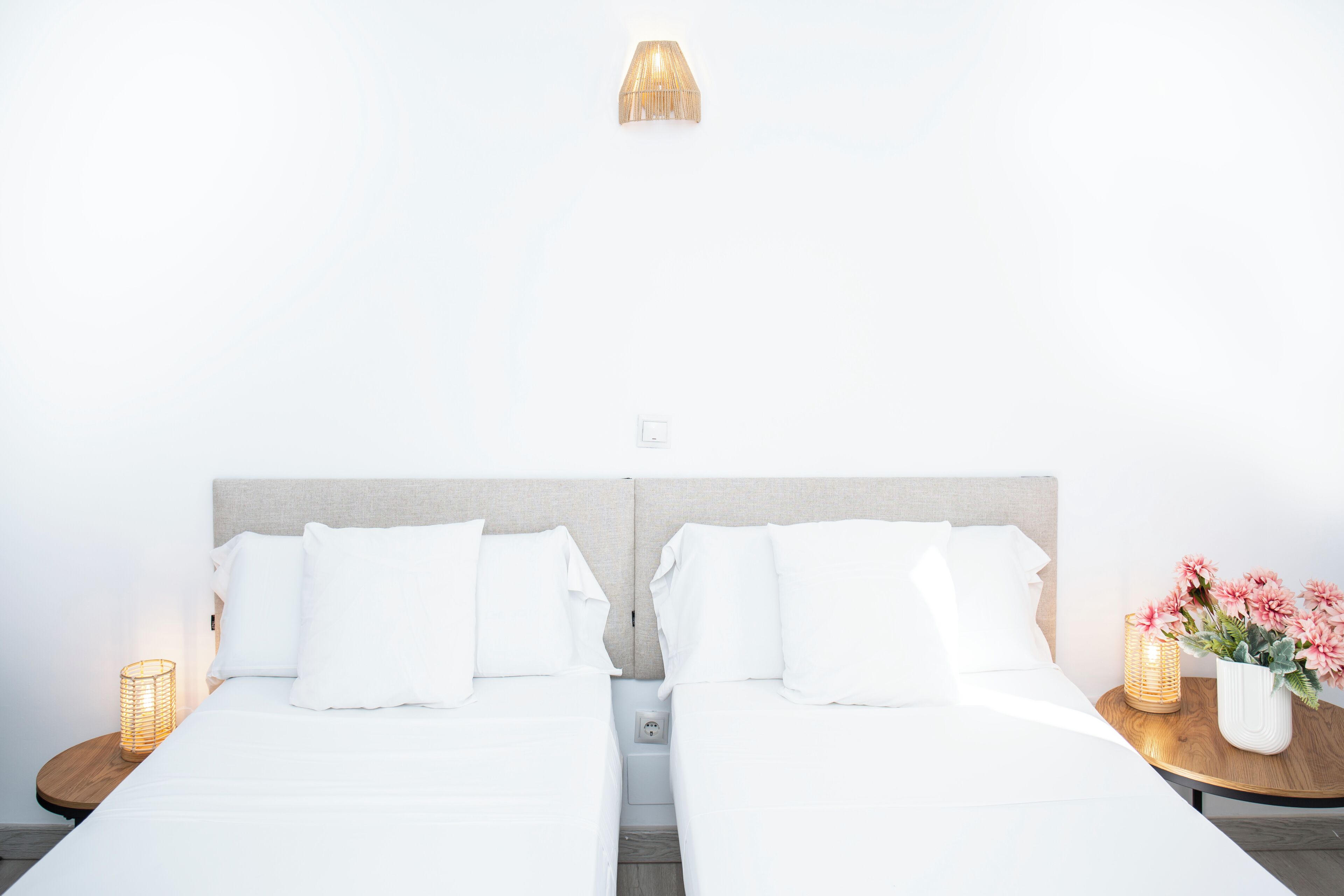 A double bed with white bedding, a headboard, a bedside lamp, and a small table with a vase of flowers.