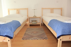 A room with two wooden beds, a small bedside table with a lamp, and a patterned rug on the floor.