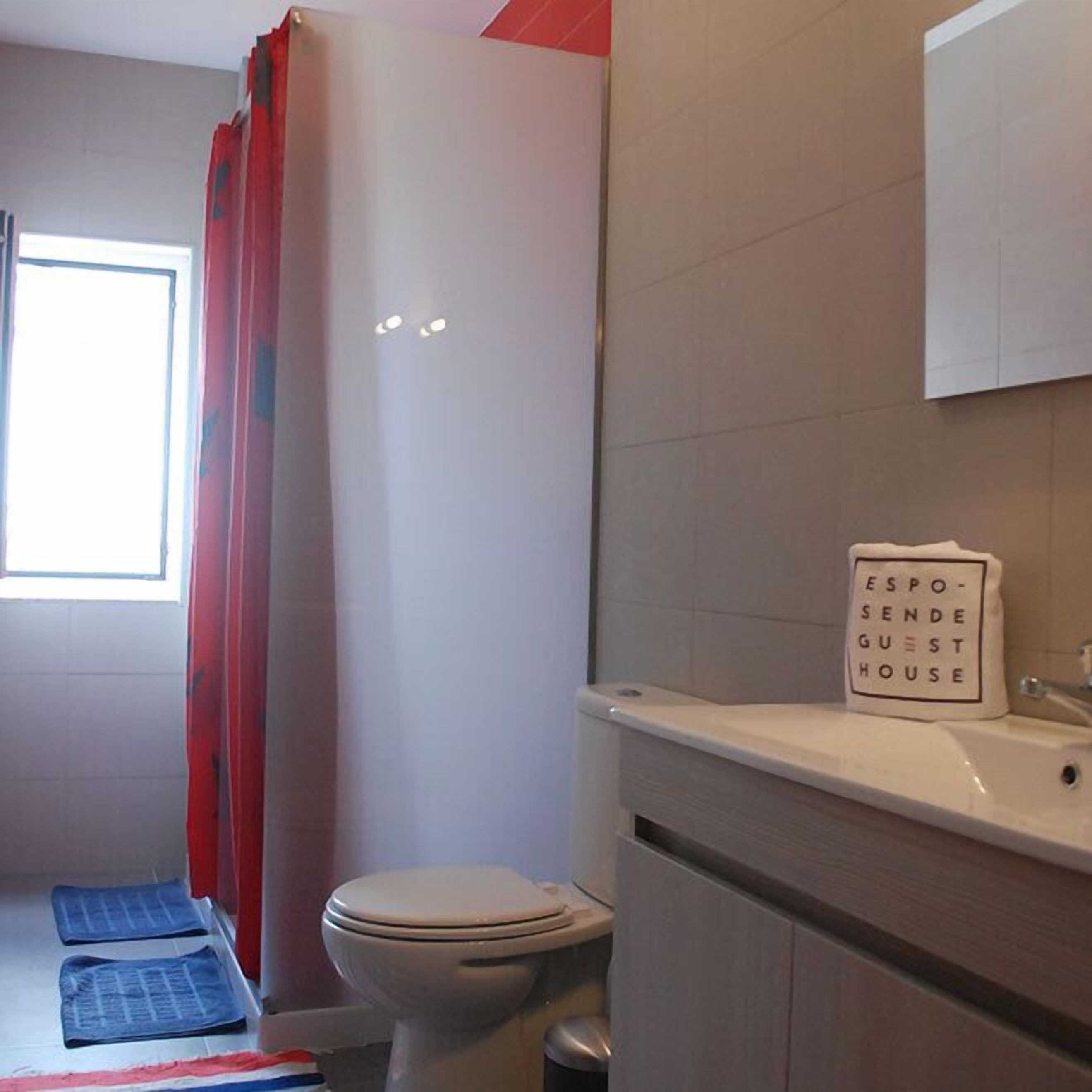 Ein Badezimmer mit Toilette, Waschbecken und Duschvorhang. An der Wand ist ein Schild mit der Aufschrift 'ESPO-SENDE GUEST HOUSE'.