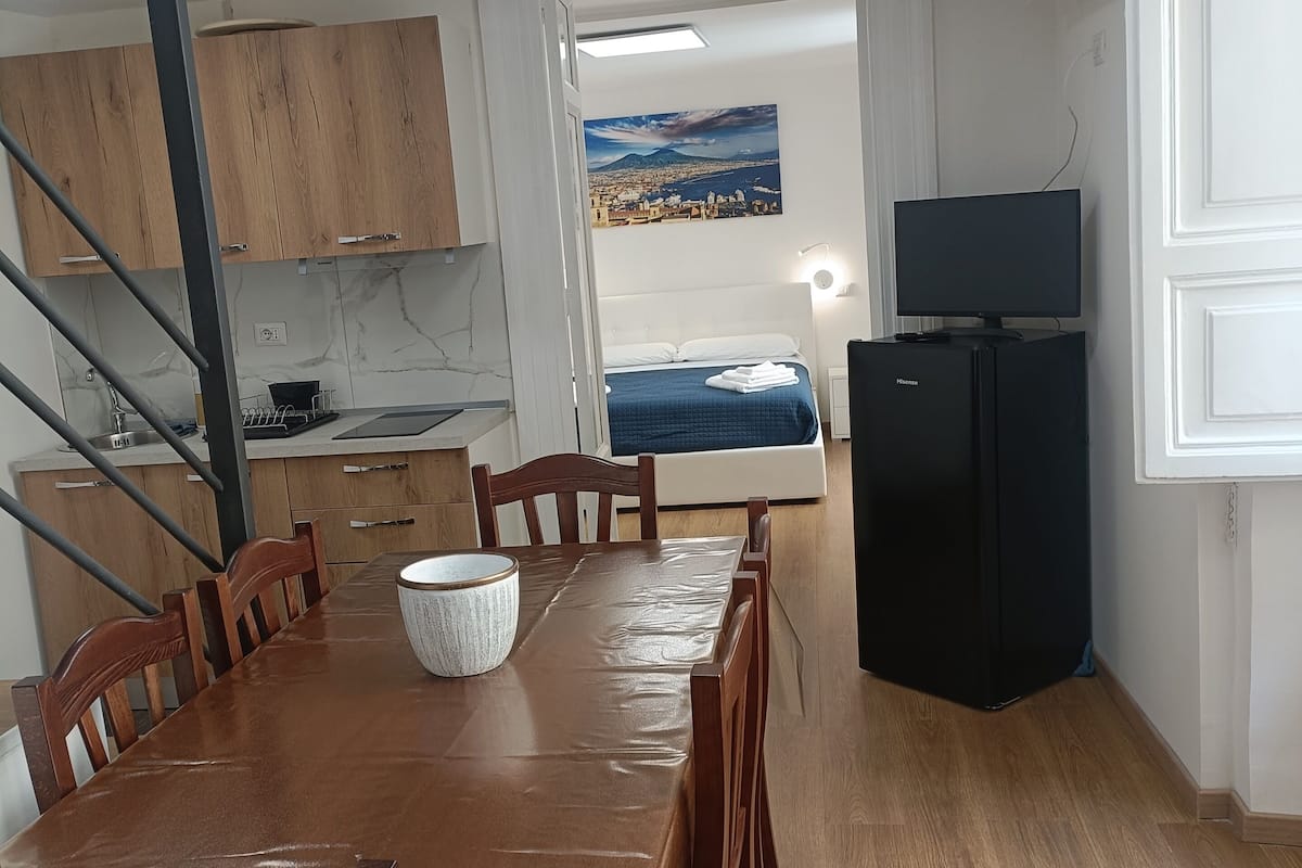 Una cocina moderna con armarios de madera, una mesa de comedor con sillas, un refrigerador y un cuadro de un paisaje urbano en la pared.