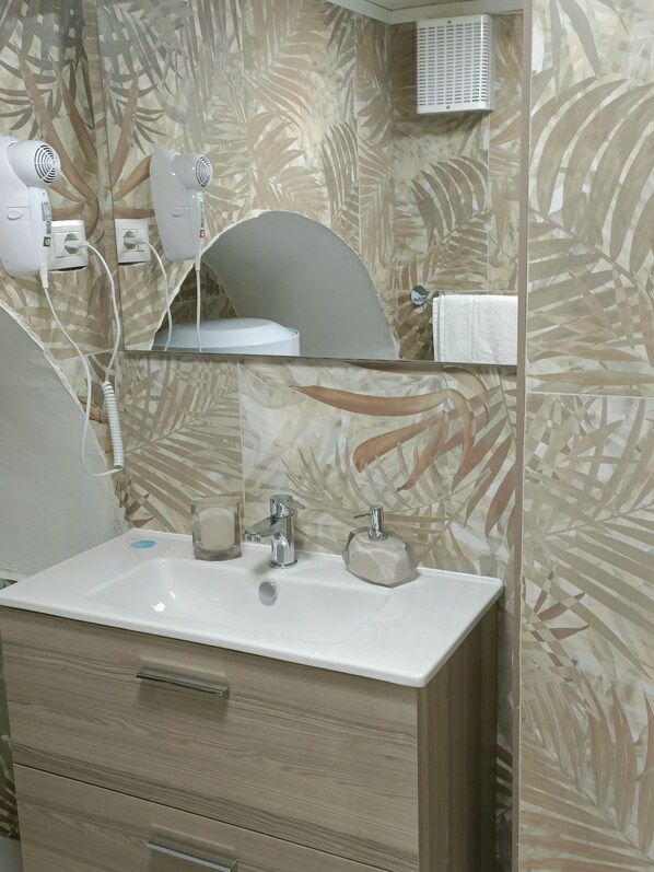 Une salle de bain avec un lavabo blanc, un miroir, un porte-serviettes et un sèche-cheveux.