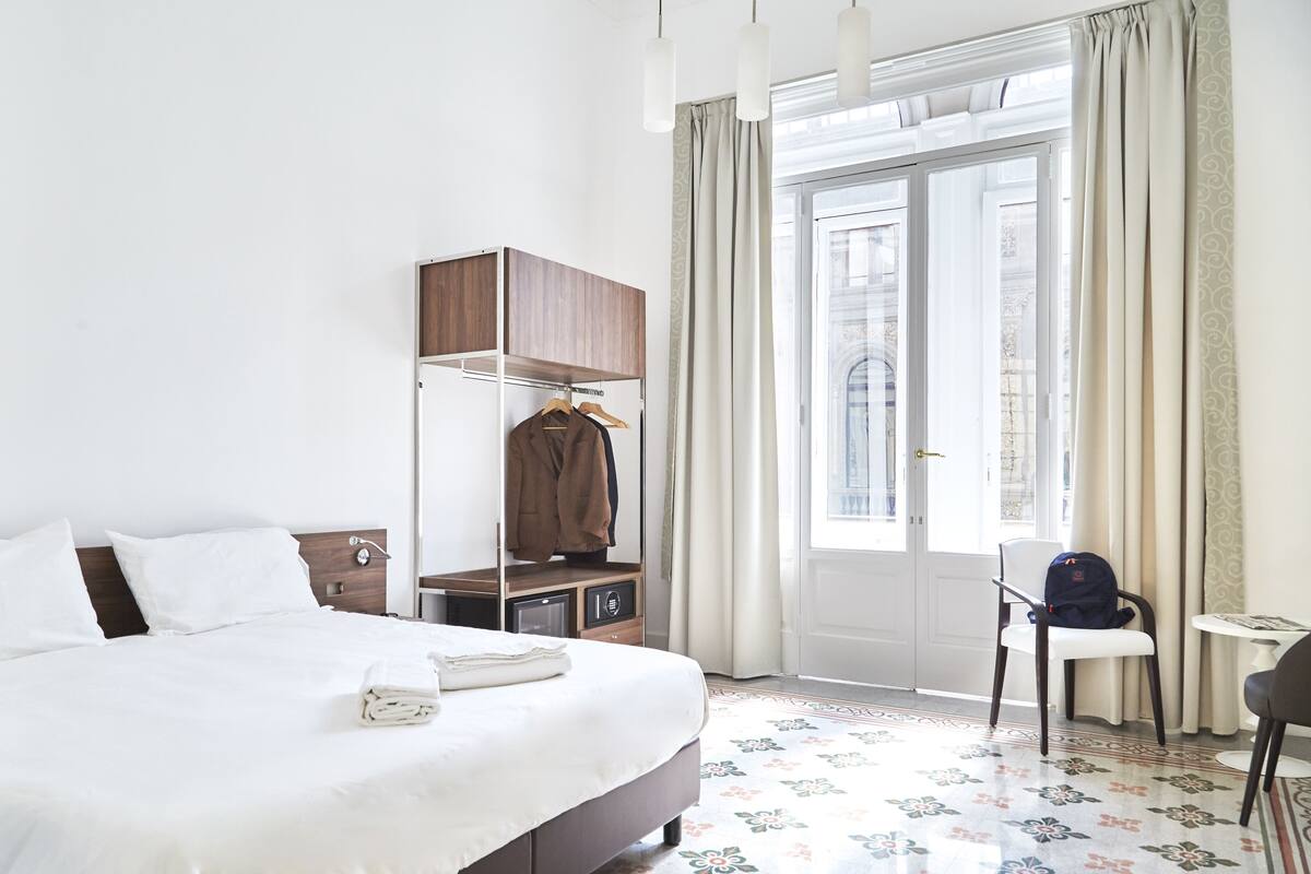 Una habitación de hotel con una cama bien hecha, un armario, una silla y una mesita.