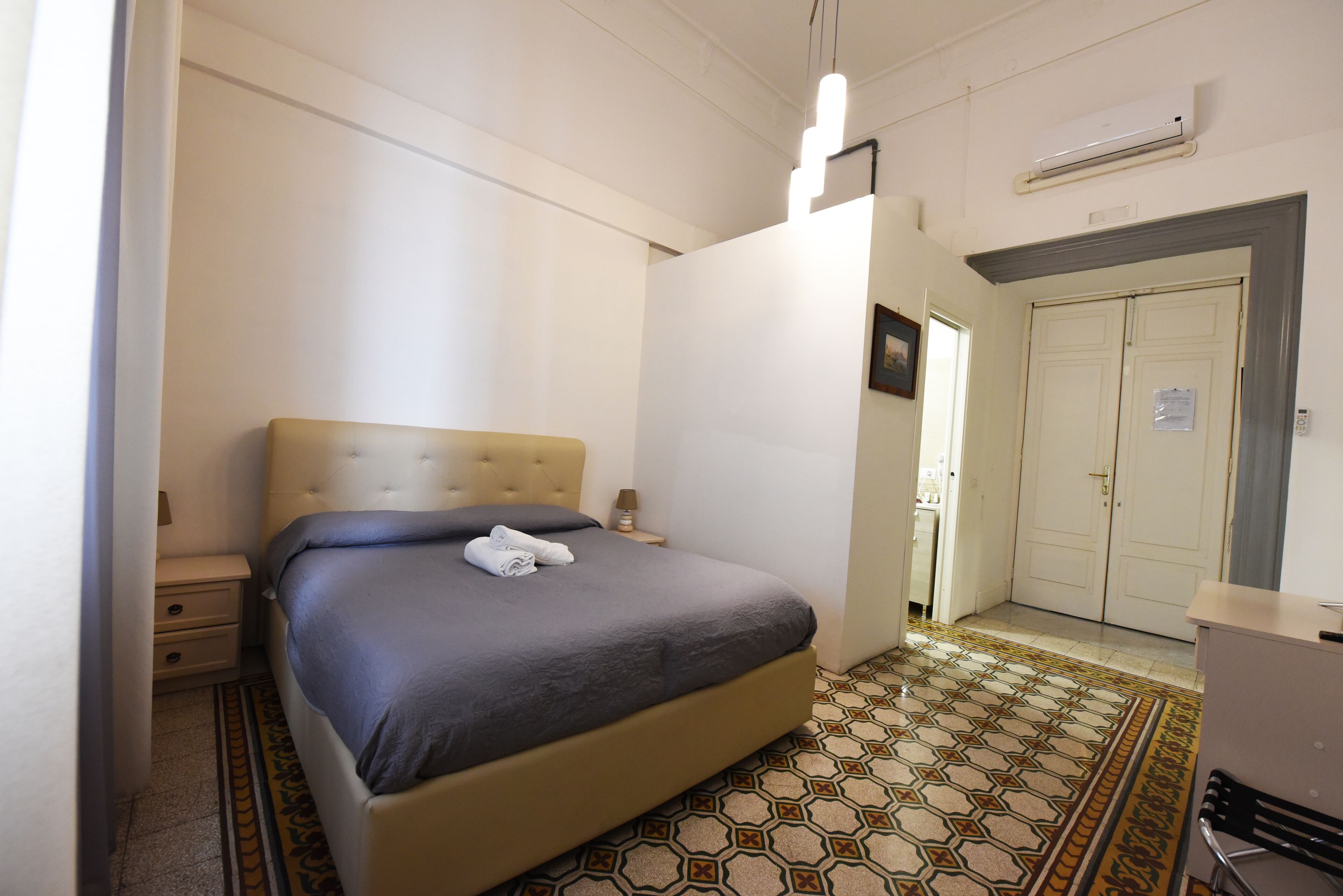 A bedroom with a bed, bedside tables, a wardrobe, and a patterned floor.