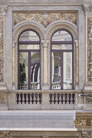 Une façade d’immeuble ornée de détails architecturaux raffinés, notamment une fenêtre décorative dotée d’une balustrade et d’une surface vitrée réfléchissante.