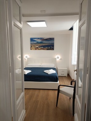 A bedroom with a bed, bedside tables, a chair, a painting, and a view of a cityscape. - Maison Toledo 210 (Naples)