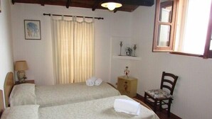Una habitación con dos camas, una silla, una mesita, una lámpara, una ventana y un cuadro en la pared.