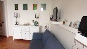 Una sala de estar con un sofá azul, un mueble blanco y adornos colgados en la pared.