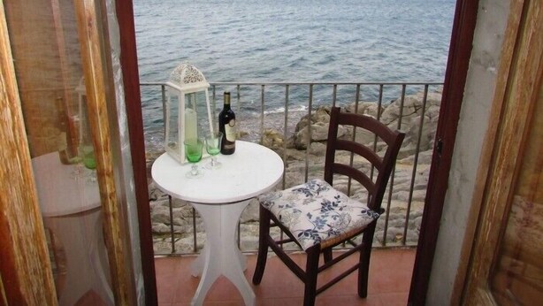 Un balcón con una mesa, una silla, una botella y un vaso.