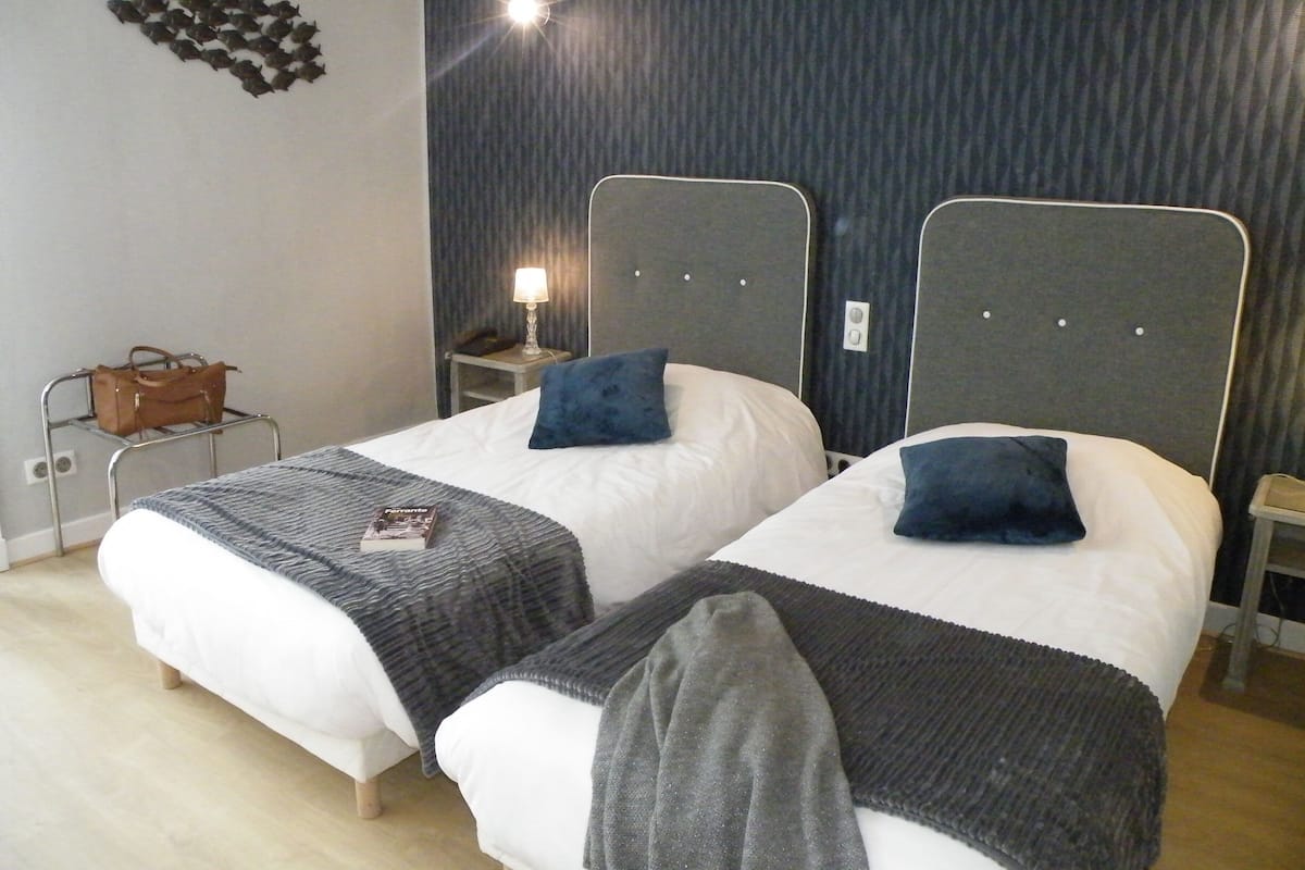 Une chambre d’hôtel avec deux lits, une table de chevet avec une lampe, une horloge murale et un sac à main posé sur un porte-manteau.