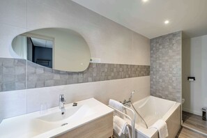 A modern bathroom with a large oval mirror, a freestanding bathtub, and a vanity with a sink. - Brit Hotel Roanne - Le Grand Hotel (Roanne)