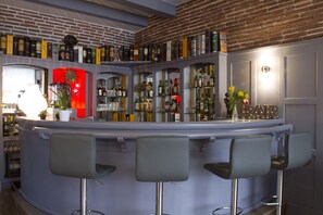 Zona de bar con pared de ladrillo, estantes llenos de botellas de licor y tres taburetes.