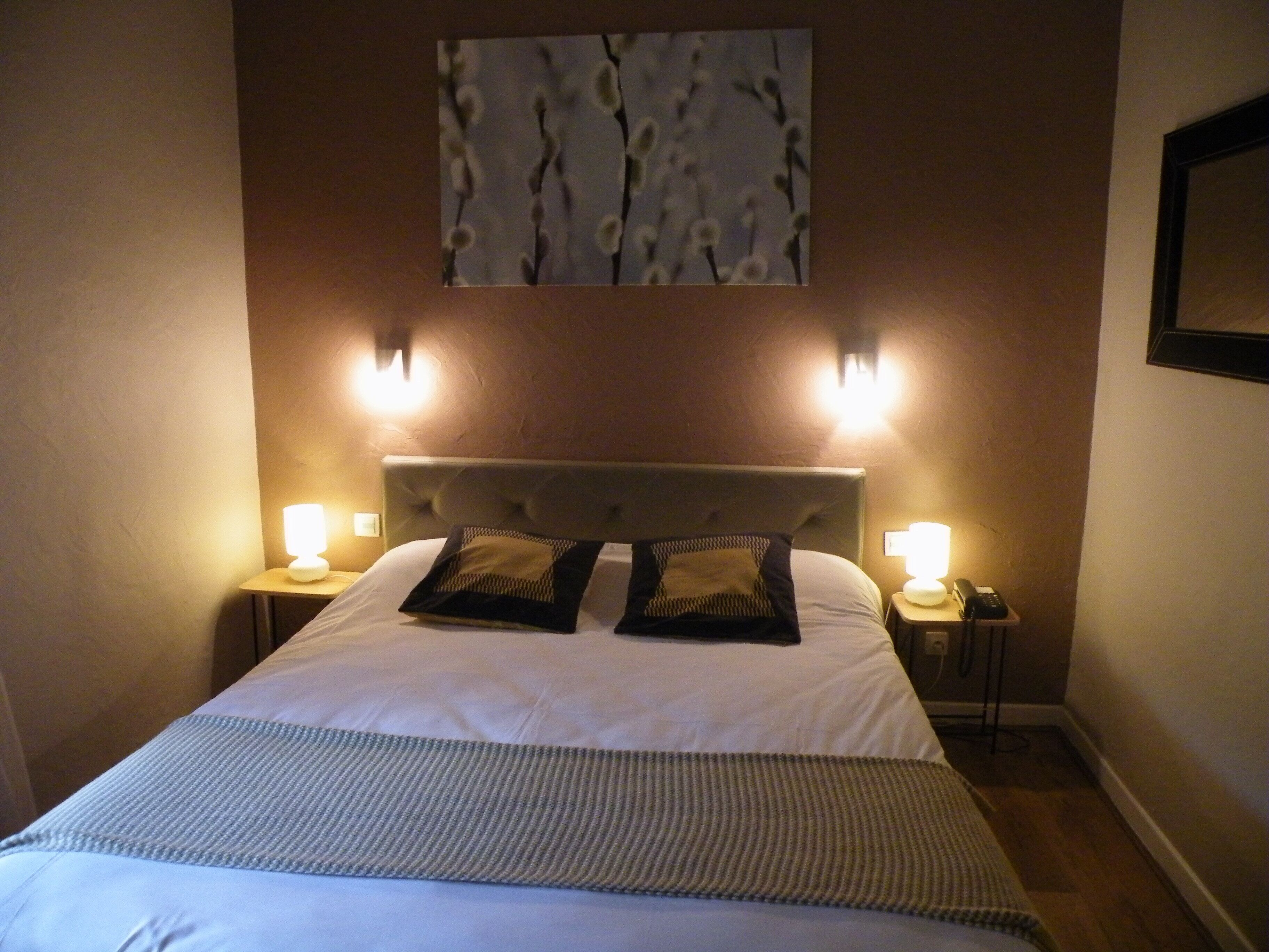 A neatly made bed with a striped blanket, two decorative pillows, and two bedside lamps.