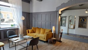 Un hall de hotel con un sofá amarillo, una mesa con sillas, una lámpara y una recepción.