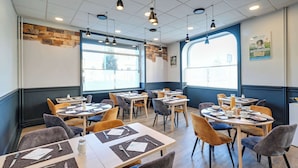 Un comedor moderno con varias mesas y sillas, ventanas amplias y una pared de acento de piedra.