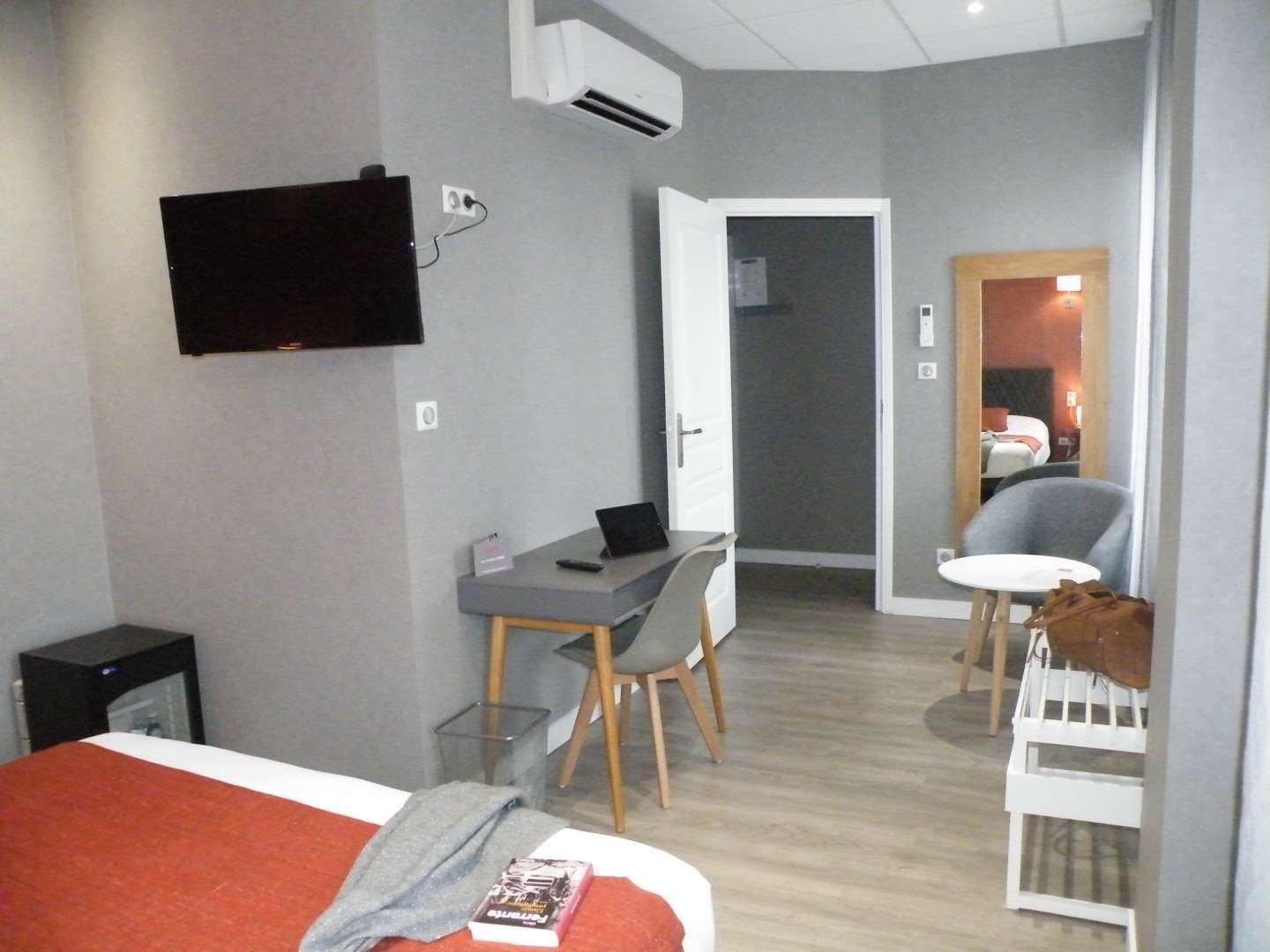 Een hotelkamer met een bed, een bureau met stoel, een aan de muur bevestigde televisie en een deur naar een badkamer.