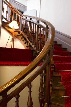 Una escalera de madera curvada con escalones alfombrados en rojo y barandilla de bronce.