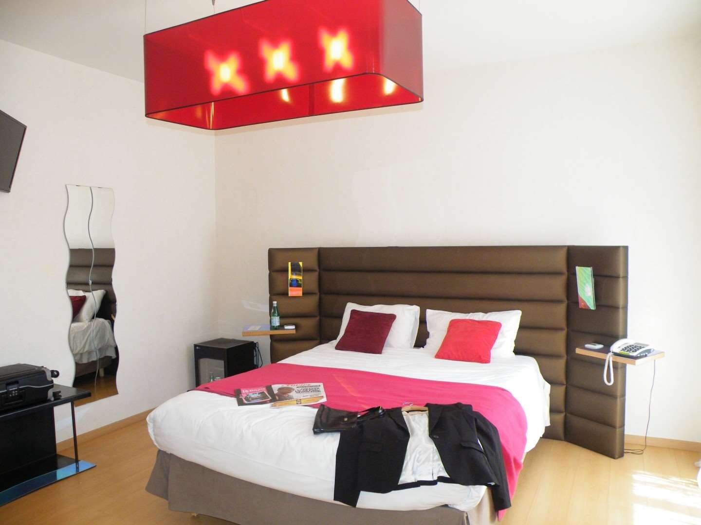 Ein Hotelzimmer mit einem Bett, einem Nachttisch, einer Lampe und einem Spiegel an der Wand.