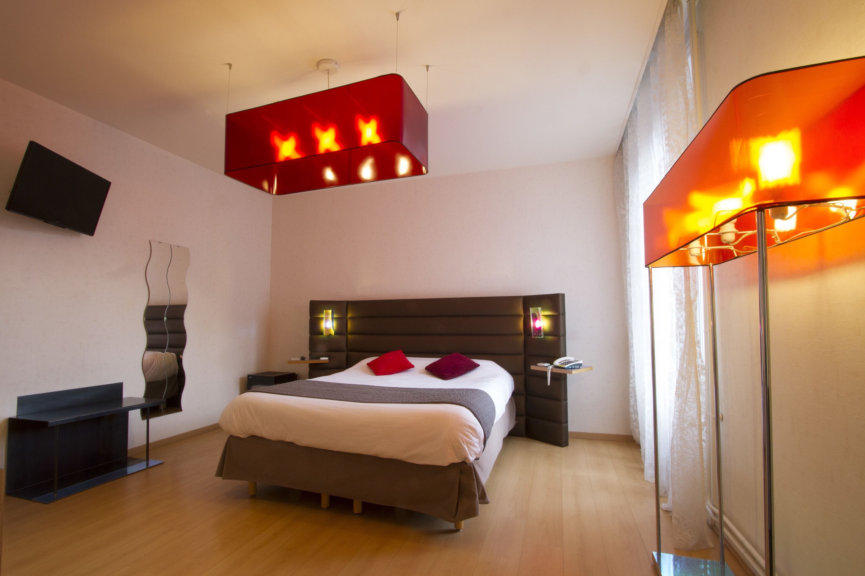 Een moderne slaapkamer met een groot bed, nachtkastjes, een televisie en een opvallende rode lamp boven het bed.