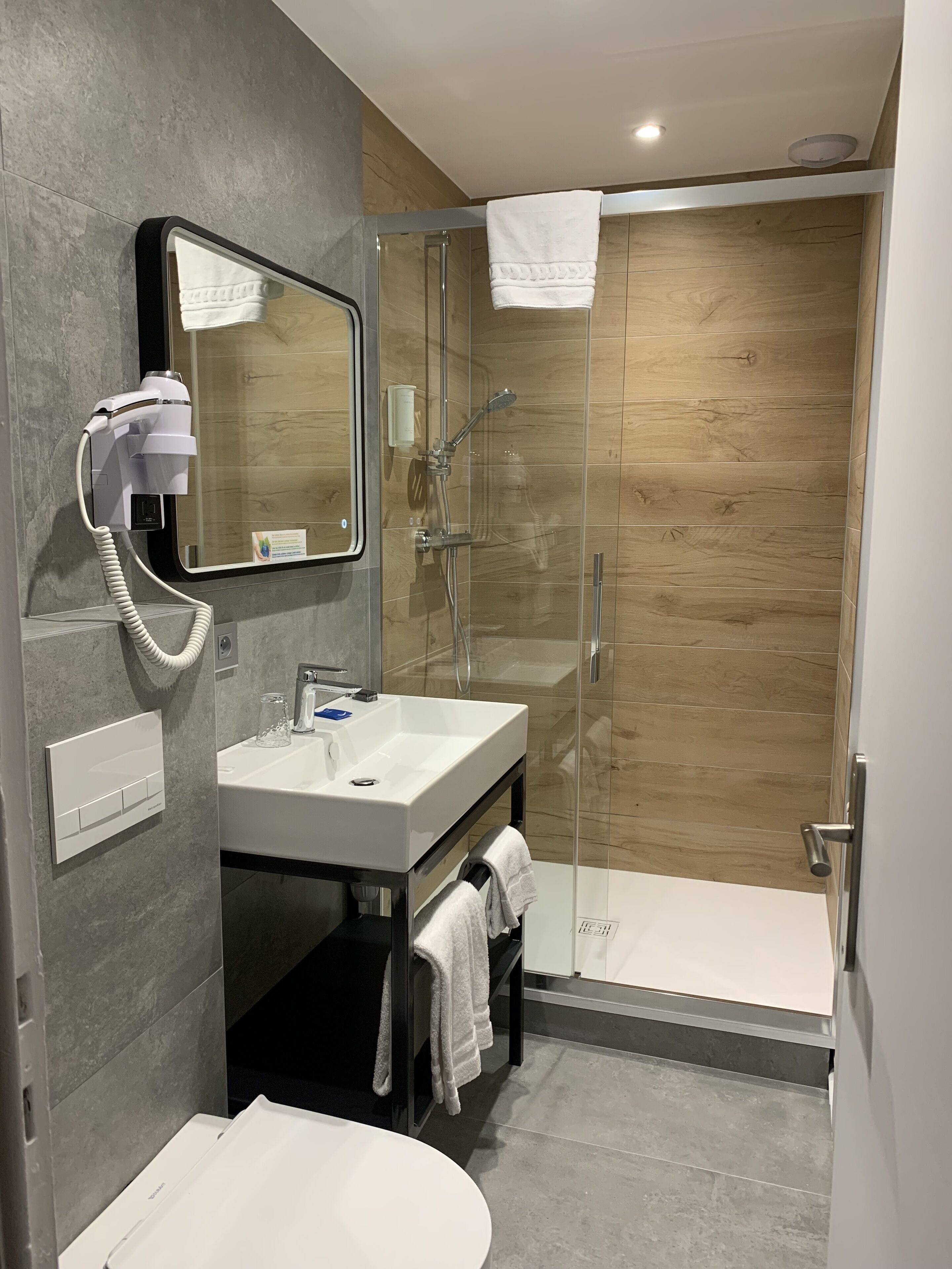 A modern bathroom with a glass-enclosed shower, a white sink, and a hairdryer mounted on the wall.