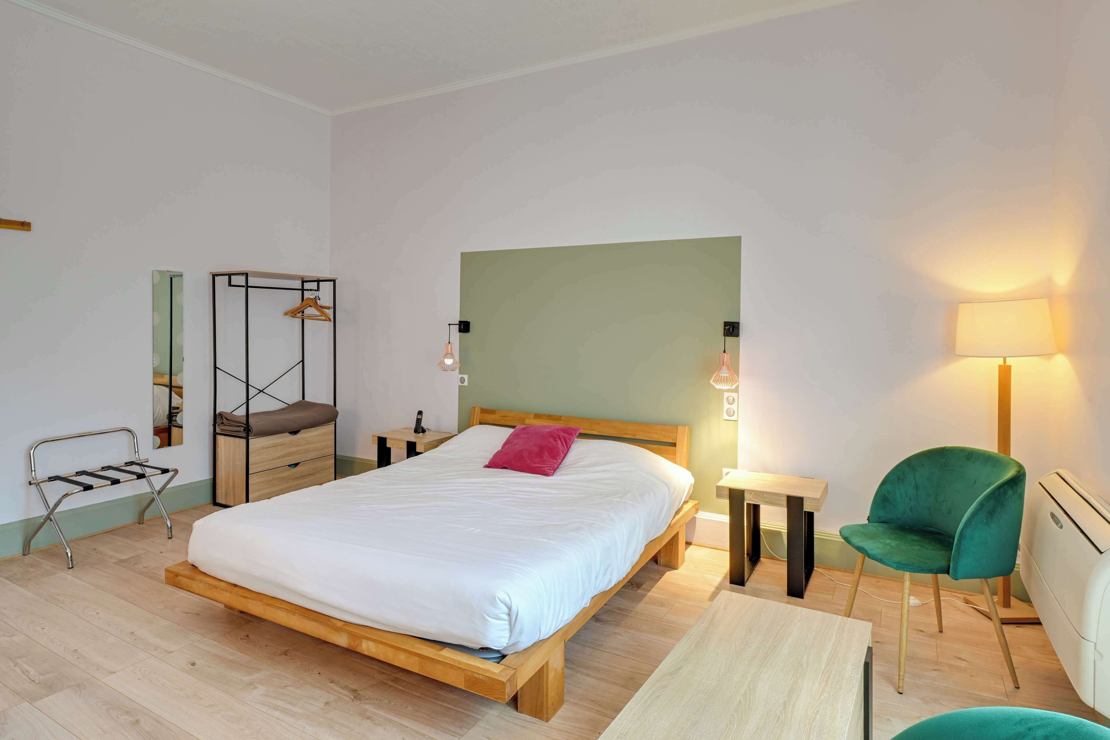 Un dormitorio moderno con una cama de madera, una silla verde, una mesita y una lámpara de noche.