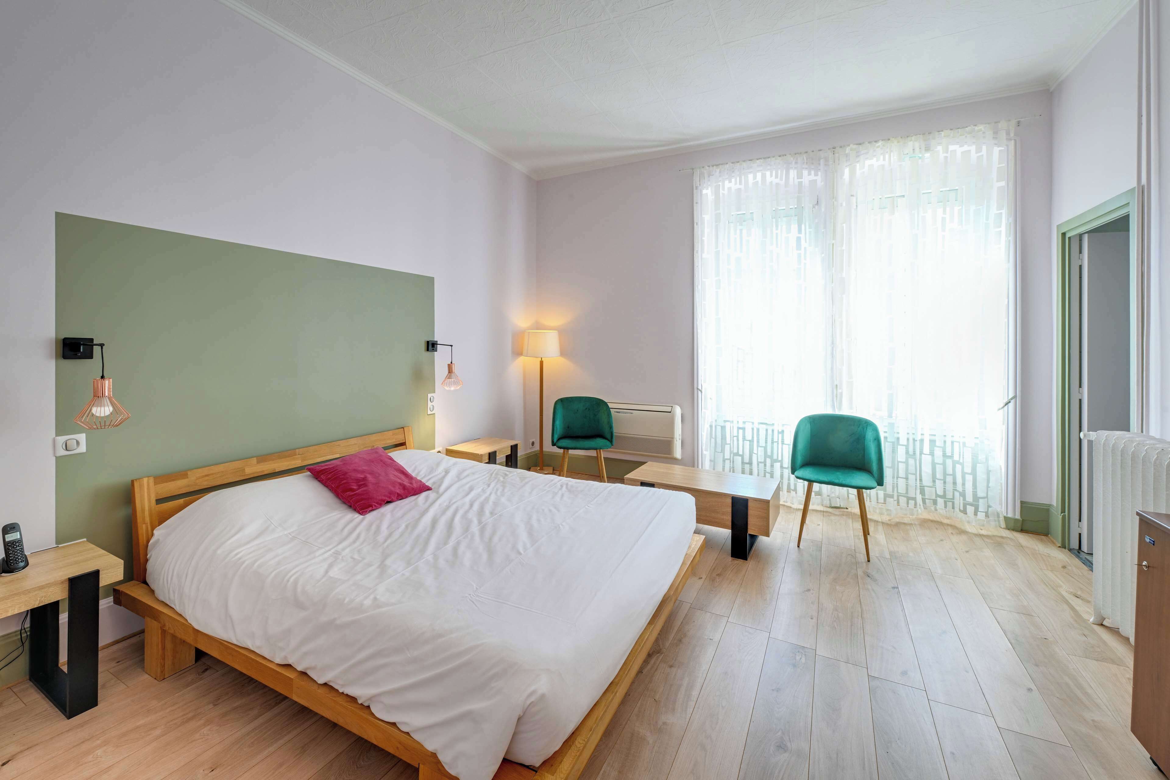 Ein Hotelzimmer mit Bett, Nachttischen, Schreibtisch, Stühlen und einem Fenster mit Vorhängen.