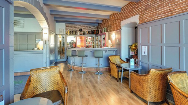 Un área de bar con sillas de mimbre, una barra y una pared de ladrillo.