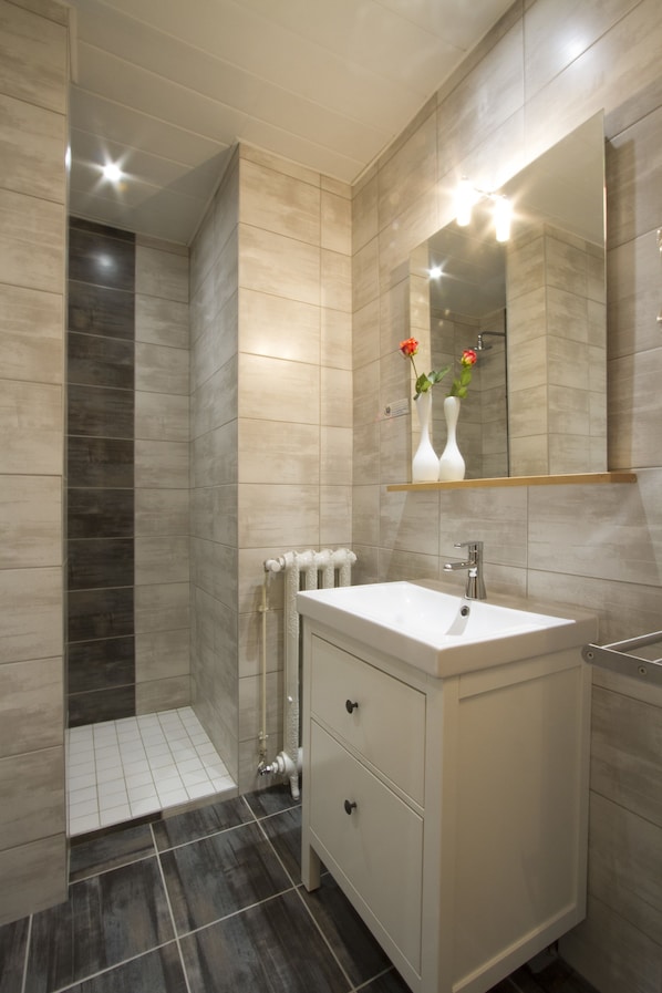 A modern bathroom with a large mirror, a white sink, and a shower area.