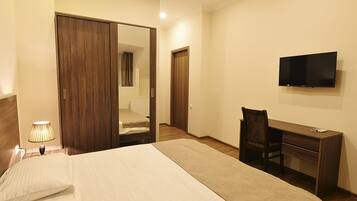 A hotel room with a bed, desk, chair, TV, and a mirror.