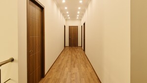 Un pasillo estrecho con suelo de madera y puertas a ambos lados, que conduce a una habitación con una puerta de madera al final.