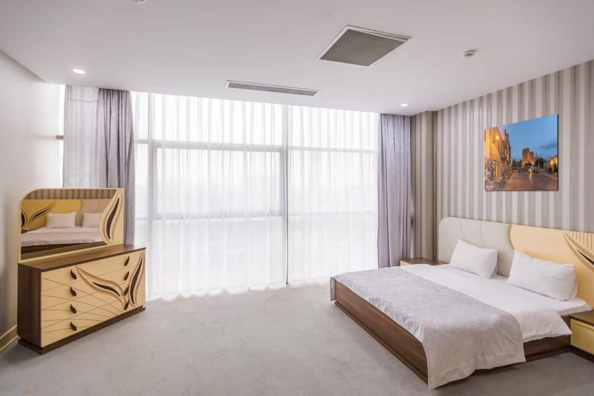 Une chambre d’hôtel avec un grand lit, une commode en bois, un tableau au mur et une vue par la fenêtre.