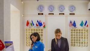 A reception desk with a sign reading "RECEPTION" above it. There are clocks on the wall and flags of various countries displayed. - Riva Hotel (Baku)
