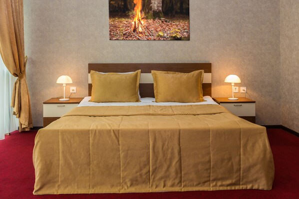 Une chambre d’hôtel avec un grand lit, deux lampes de chevet, une tête de lit et un tableau représentant un feu de camp accroché au mur.