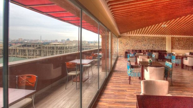 A spacious balcony with a view of a cityscape, furnished with tables and chairs, and a stone wall with a geometric pattern. - Riva Hotel (Baku)
