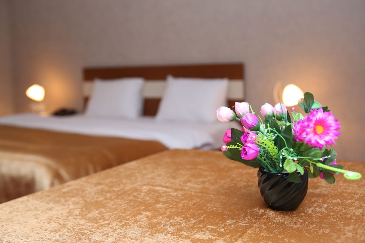 Une chambre d’hôtel avec un lit, une table de chevet et un vase de fleurs posé sur une table.