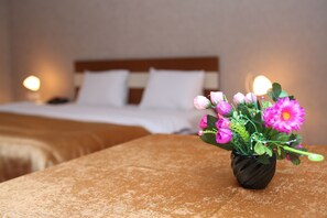 A hotel room with a bed, a nightstand, and a vase of flowers on a table. - Riva Hotel (Baku)