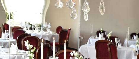 A dining area with tables set for a meal, featuring crystal candle holders and white tablecloths.