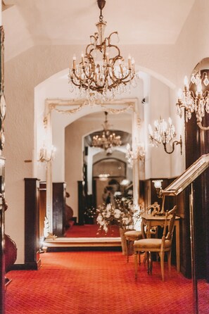 A grand hallway with a red carpet, ornate chandeliers, and a mirror reflecting a staircase. - Miramar Hotel (Sylt)