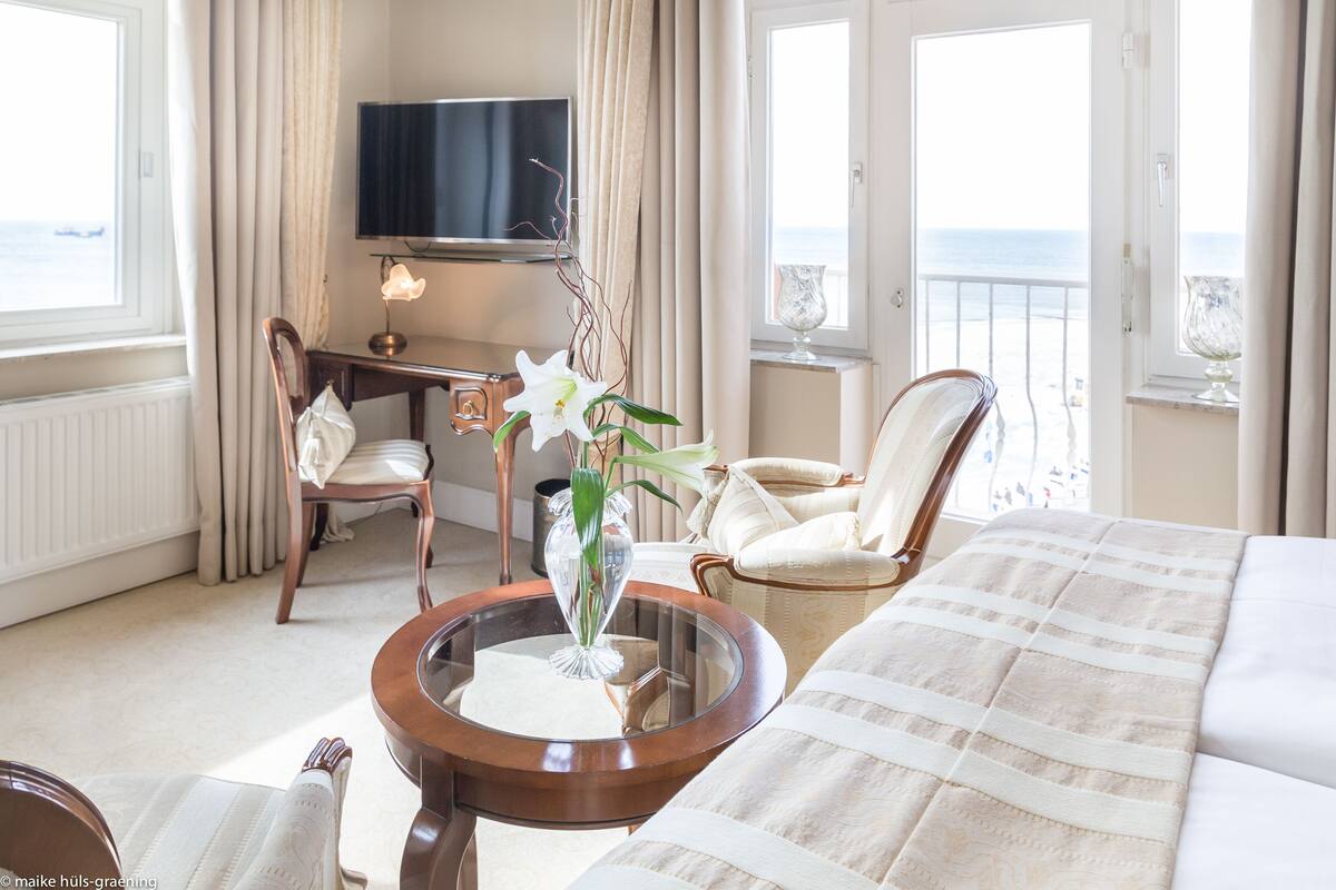 A hotel room with a bed, a desk, a chair, a TV, and a view of the sea.
