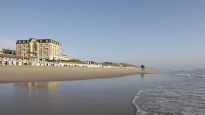 Un hotel frente a la playa con un edificio grande, una playa de arena y el océano.