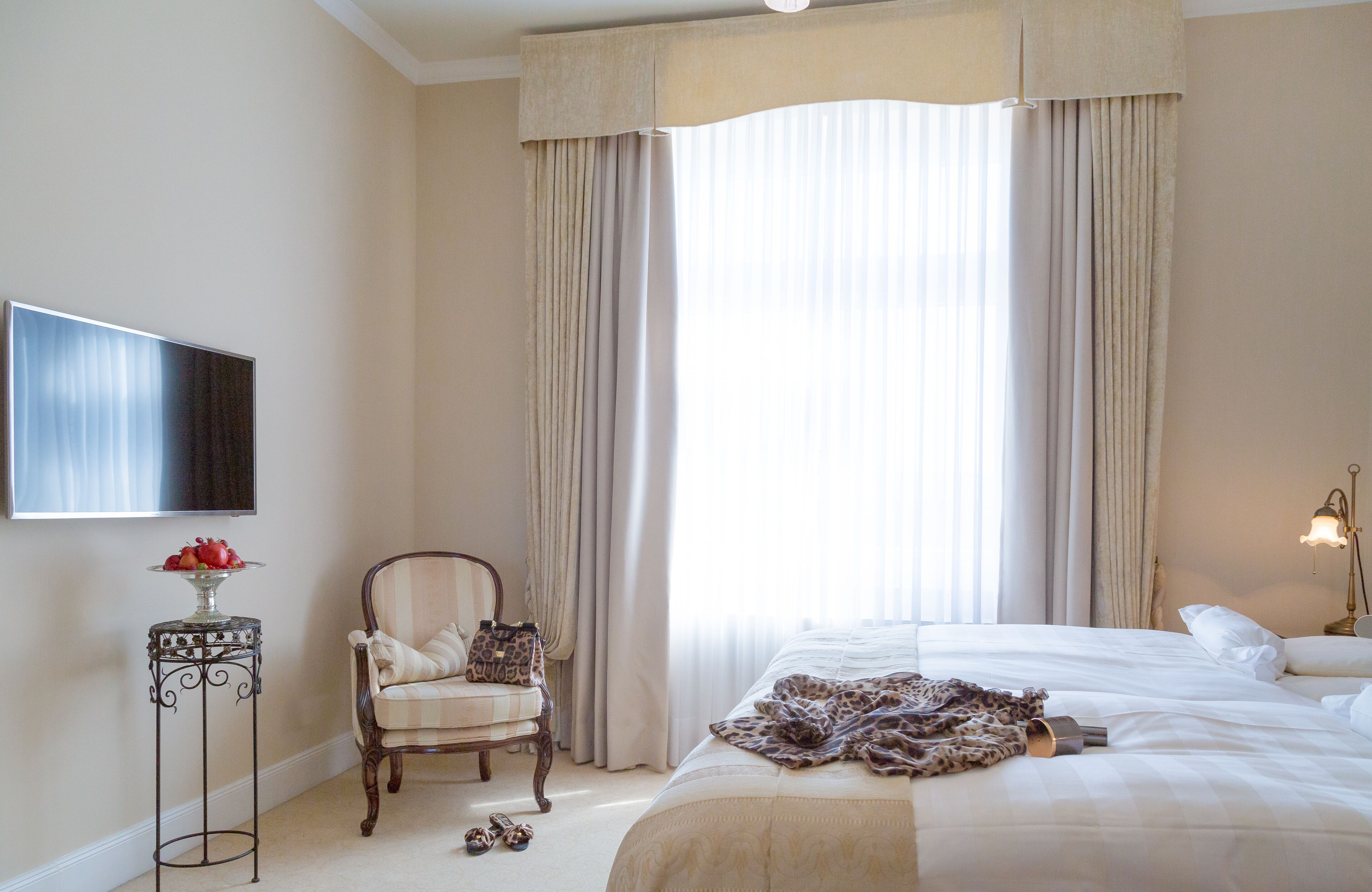 A hotel room with a large bed, a chair, a small table with fruit, and a TV on the wall.