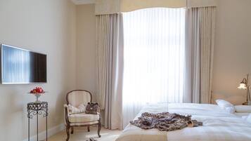 A hotel room with a large bed, a chair, a small table with fruit, and a TV on the wall.