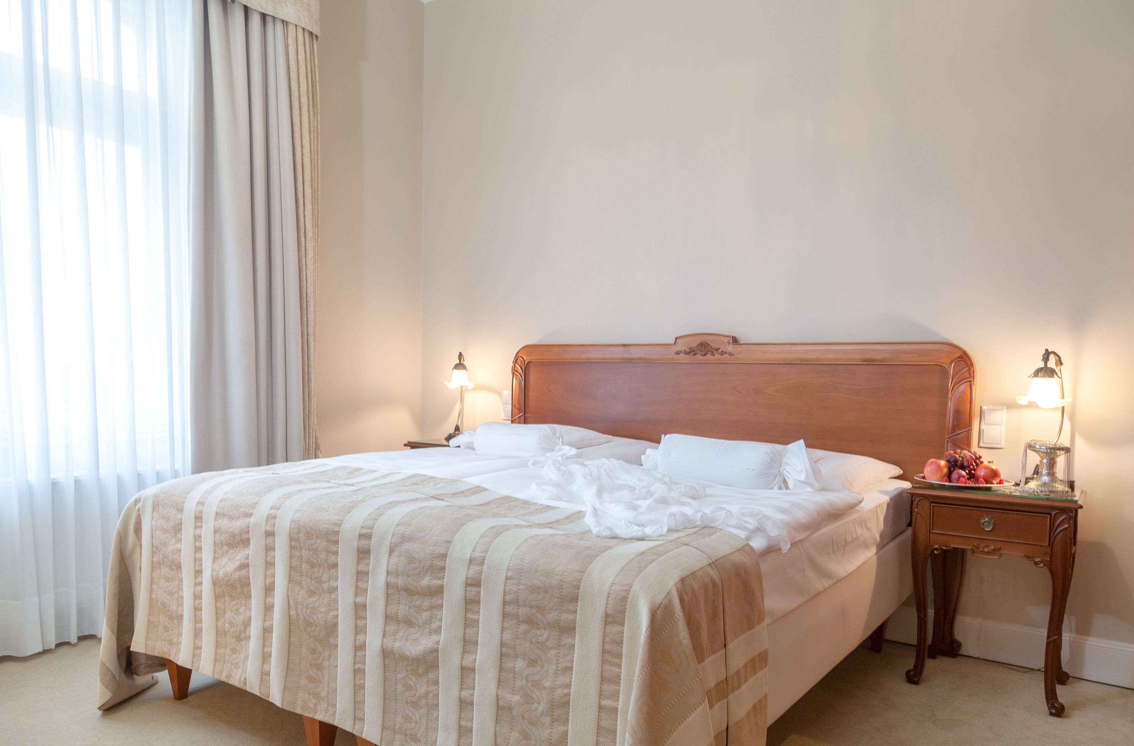 A neatly made bed with a striped bedspread, two bedside lamps, and a nightstand with a fruit bowl.