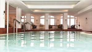 Una piscina interior con agua cristalina, rodeada de zonas de estar y amplias ventanas.