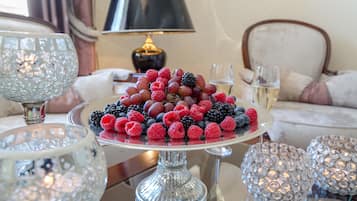 A dining table with a fruit platter, crystal glasses, and a lamp in the background.
